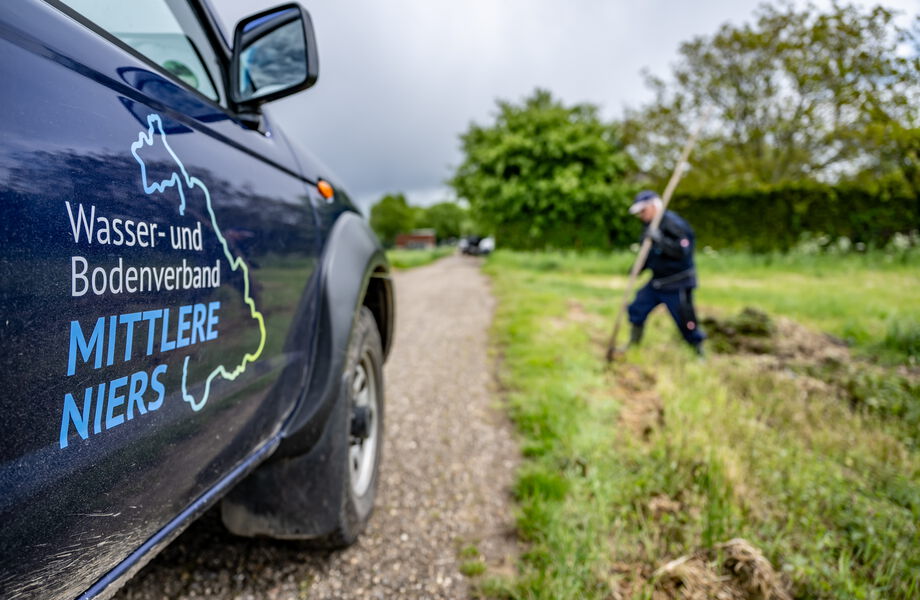 Fahrzeug des Wasser- und Bodenverbands, im Hintergrund ein Mitarbeiter bei Pflegearbeiten.