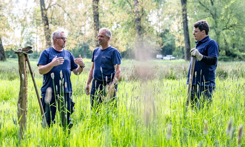 Drei Mitarbeiter des Wasser- und Bodenverbands im Austausch während Arbeiten auf einer Grünfläche.